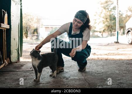 The concept of small business, feminism and women's equality. A young female car mechanic strokes a cat, in the background a street. Close up. Stock Photo
