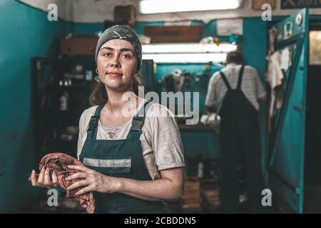 The concept of women's equality and feminism. A woman in a work uniform wipes her hands with a rag. In the background, a man is working at a machine. Stock Photo