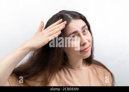 Dandruff and seborrhea. A young woman with dark hair, brushing dandruff from her hair with her hand. Gray background. The concept of hair problems and Stock Photo