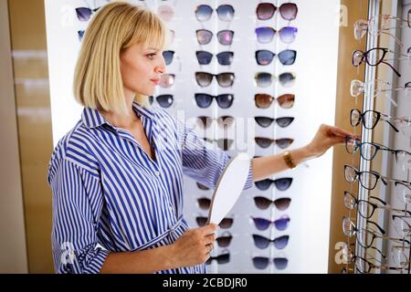 Health care, eyesight and vision concept. Happy woman choosing glasses at optics store Stock Photo