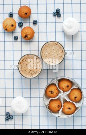Two cups of foamy latte and muffins, blueberries, marshmallows on a checkered tablecloth. Breakfast concept. Flatlay design Stock Photo