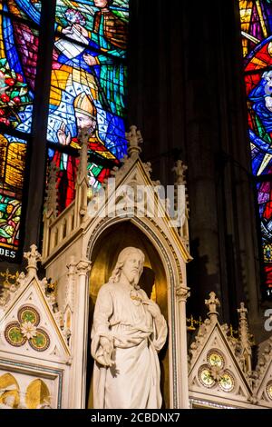 A marble carved statue of Jesus Christ in front of stained glass windows inside the Votivkirche, Votive church. In Vienna, Austria. Stock Photo