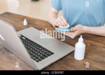Close-up of hands of unrecognizable woman wiping with antibacterial sanitizer display of cell phone Stock Photo