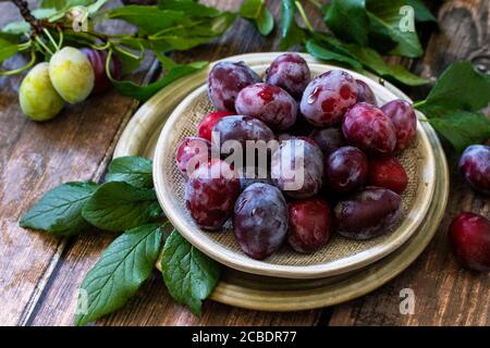 Ripe juicy plums in a bowl on a wooden background. Stock Photo