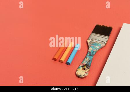 Top view of a blank white canvas with a stained paintbrush and colorful chalks on a red background Stock Photo