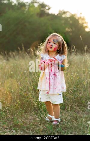 the little girl was covered in paint. a girl in a green clearing. hair up. Stock Photo