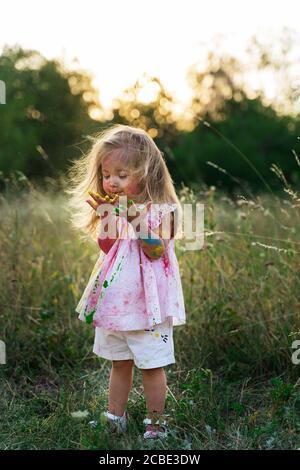 the little girl was covered in paint. a girl in a green clearing. hair up Stock Photo