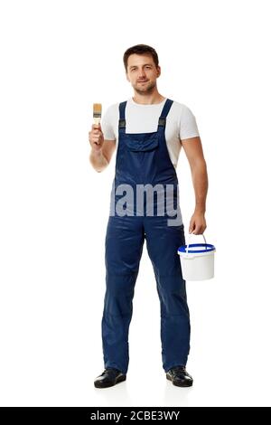 caucasian repairman in blue uniform holding paint brush and can with paint. builder or painter decorator isolated on white background Stock Photo
