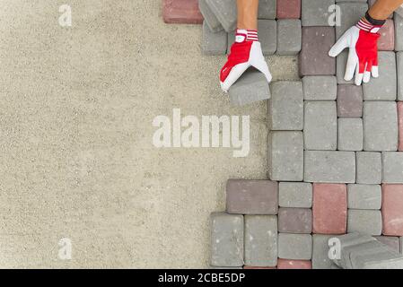 worker laying paving stones. stone pavement, construction worker laying cobblestone rocks on sand. Stock Photo