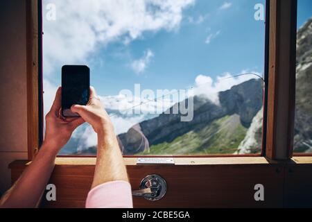 View from window of cogwheel train. Man photographing mountains above clouds in Switzerland. Stock Photo