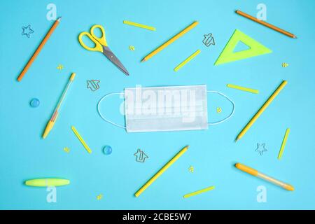 Stationery on blue. Bright stylish flat lay. Different yellow tools with white protective mask in centre. Stock Photo