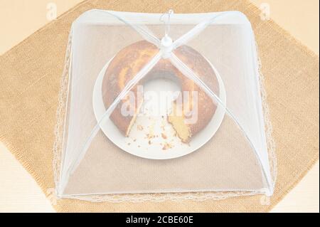 Cornmeal Cake (Bolo de Fuba) cut Brazilian style on a white plate with food net cover. Isolated on jute. Top view. Horizontal shot. Stock Photo