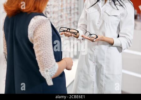 woman in white coat holding glasses in palms, offering sale on the second pair of glasses, present concept, bargain concept, close up cropped photo Stock Photo