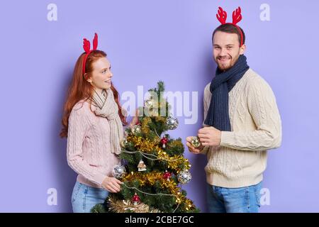 Charming young unshaven man wearing casual blue jeans and comfortable sweater, having stylish scarf on neck and red funny headband, smiling happily, g Stock Photo