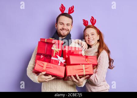 Portrait of loving pretty couple posing over light coloured background , carrying various beautiful gifts in hands, looking at camera, smiling brightl Stock Photo