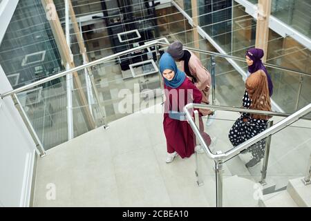 Young muslim cheerful business traveller women in national arabian clothings visiting business centre, coming up the stairs chatting about their futur Stock Photo