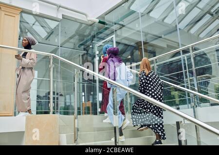 Multiracial group of muslim business women visiting international conference at business centre, walking up the staircase sharing impressions and idea Stock Photo