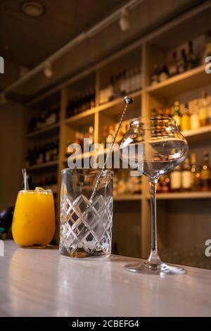silver cocktail shaker lying on yellow background with ice cubes and tall glass, horizontal format Stock Photo