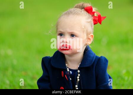 a young girl sits with a smeared face in red lipstick Stock Photo