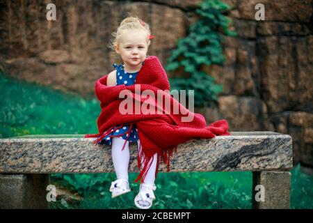 a young girl on a bench is wrapped in a woolen blanket. Stock Photo
