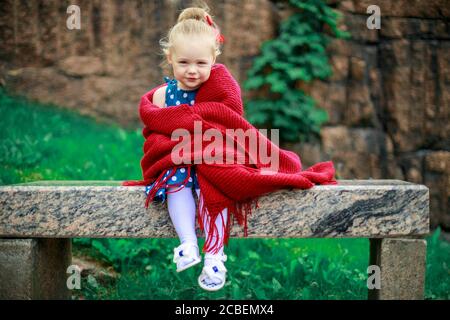 a young girl is sitting on a bench wrapped in a woolen blanket. Stock Photo