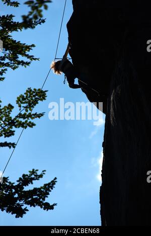 Vertical snapshot of female rock-climber, climbing up a cliff, wearing blue  leggings and a black