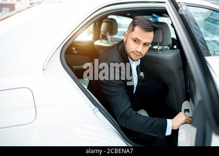 Confident young business male getting out from white executive car, from rear passenger seat Stock Photo