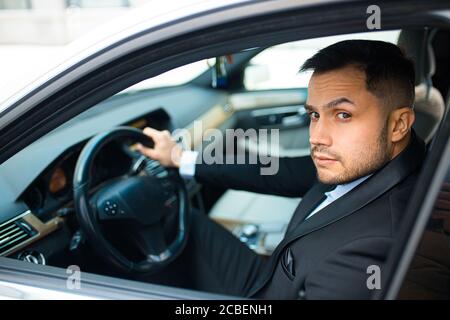 young bearded male behind wheel in his executive car, driving car Stock Photo