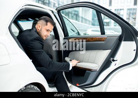 Confident young business male getting out from white executive car, from rear passenger seat Stock Photo