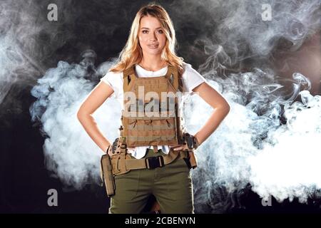 Brave amazing army girl wearing military plate carrier upon white t-shirt. Female ranger posing isolated on black studio background Stock Photo