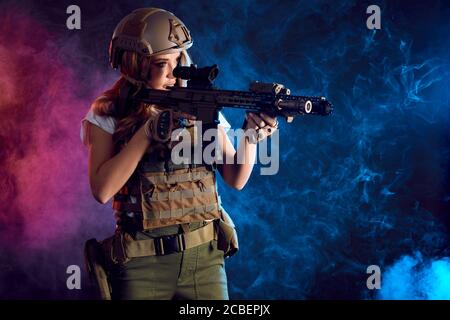 woman sniper in body armour with SVD sniper rifle. Female serving in Army, soldier with machine gun. Shot in studio. Smoky dark background imitating e Stock Photo