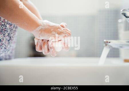 Little girl washes hands with bar of soap in washbasin under running tap water. Close up, detail Stock Photo