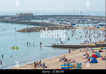 Lyme Regis, Dorset, UK. 13th Aug, 2020. UK Weather: Holidaymakers, families and beachgoers enjoy the last of the hot, hazy sunshine at the seaside resort of Lyme Regis as conditions are set to become more humid and muggy with thundery showers forecast into the weekend. Credit: Celia McMahon/Alamy Live News Stock Photo