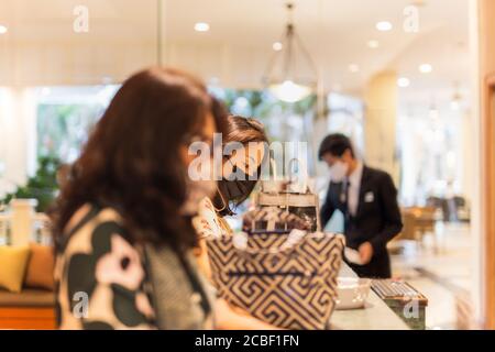 Woman client signing hotel contract paper at reception desk In face mask. Stock Photo