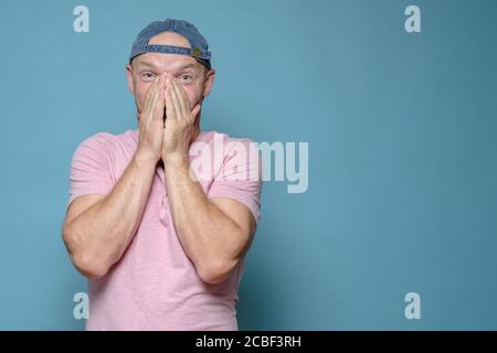 Man is shocked by a pleasant surprise, he covers mouth with hands in amazement and looks at the camera. Copy space.  Stock Photo