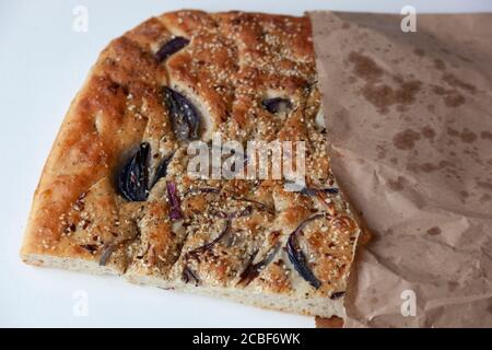 A large piece of freshly baked foccacia topped with red onion slices and sesame seeds in a takeaway paper bag Stock Photo