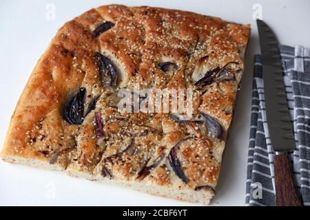 A large piece of freshly baked foccacia topped with red onion slices and sesame seeds on a white ground Stock Photo