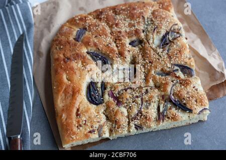 A large piece of freshly baked foccacia sliced and topped with red onion and sesame seeds on a takeaway paper bag Stock Photo
