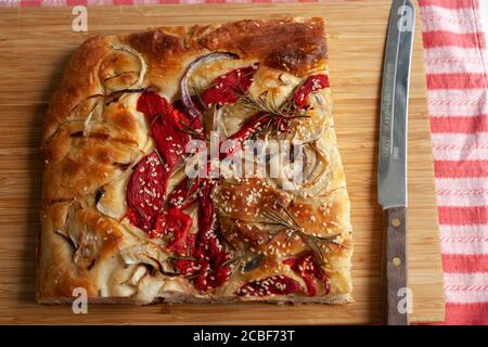 A large piece of freshly baked foccacia topped with red peppers, onions, sesame seeds and rosemary Stock Photo