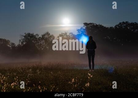 A person with a flashlight on a foggy meadow, with a flashlight in the fog, foggy meadow with moonlight Stock Photo