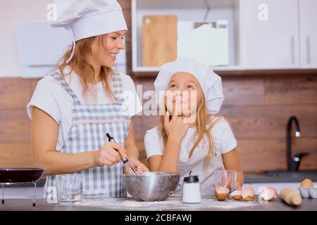 caucasian mother and daughter bake together, make dough and use ingredients need for it. Happy teamwork in kitchen of woman and her child Stock Photo