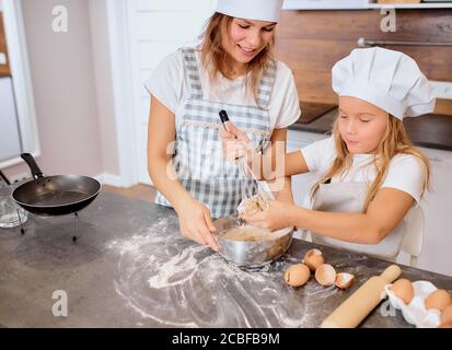 caucasian child making dough with the use of mixer with mother in kitchen at home, use chicken eggs and flour . Prepare ingredients for baking Stock Photo