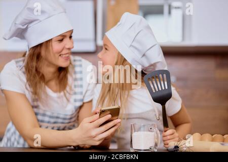 baking, cooking concept. beautiful mother and daughter child look at each other with love, going to bake in kitchen
