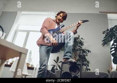 Young man plays guitar and sings a song at home with electric guitar Stock Photo