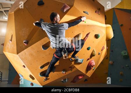 Full length back view of young physically challenged climber trying to reach top of difficult artificial climbing wall, wearing comfortable sportswear Stock Photo
