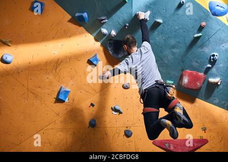 Unrecognizable powerful boulderer with physical disability hanging at climbing wall, balancing on one hand, has sporty muscled body, strong-willed, lo Stock Photo