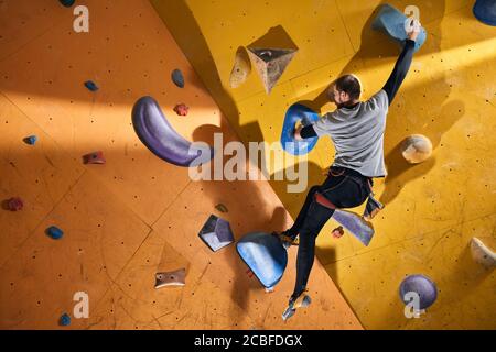 Physically challenged man stuck at difficult rock wall, thinking where to put his hand and feet to pass problem place, dressed in comfortable sport cl