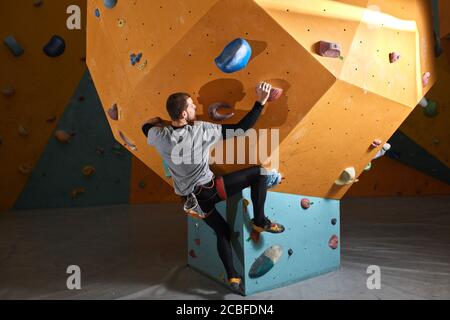 Strong sporty man with physical disability climbing steep rock artificial wall at the indoor bouldering gym, training hard, doing his best. Extreme sp Stock Photo