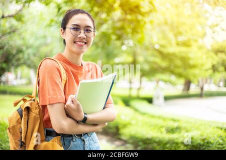 Portrait of nerd Asian woman girl smart teen happy smiling with glasses at green park outdoor in university campus with copyspace Stock Photo