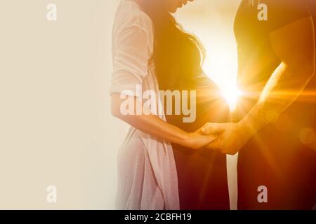 Praenant wife couple lover standing holding hand care together wtih sunshine for always stand by me and be good love forever concept. Stock Photo